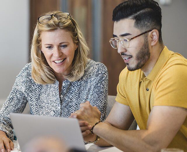 Two people looking at a laptop, smiling, in a collaborative work setting.