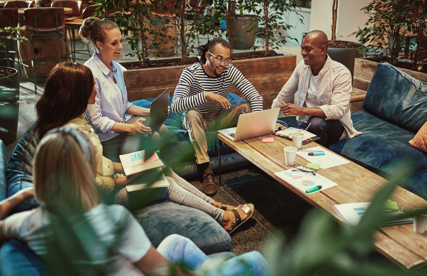 Group of people in casual setting, discussing, looking at laptop and papers on a coffee table.