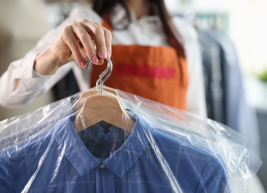 A woman is putting a shirt on a hanger wrapped in plastic.