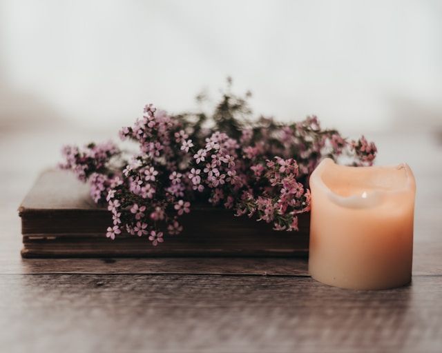 Lit candle beside small flowers on wooden surface, symbolizing remembrance, cremation services Bainb