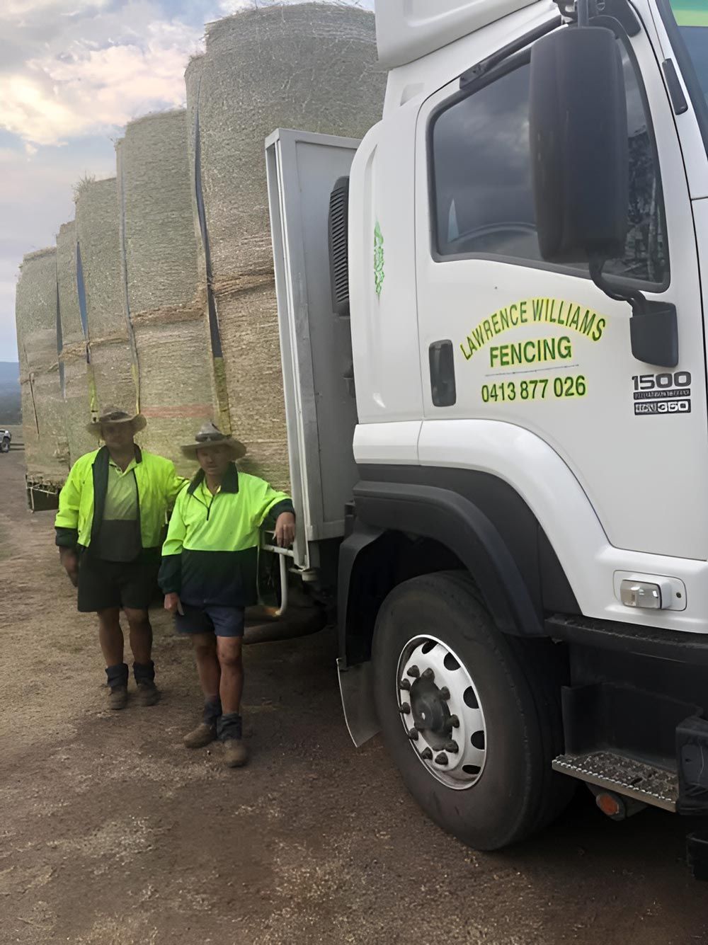 Two Men Are Standing Next To A Truck Filled With Hay Bales — Lawrence Williams Fencing in Goolmangar, NSW