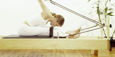A woman is doing stretching exercises on a pilates machine.