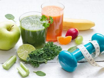 A dumbbell with a measuring tape around it is surrounded by fruits and vegetables.