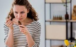 A woman in a striped shirt is smelling a bottle of essential oil.