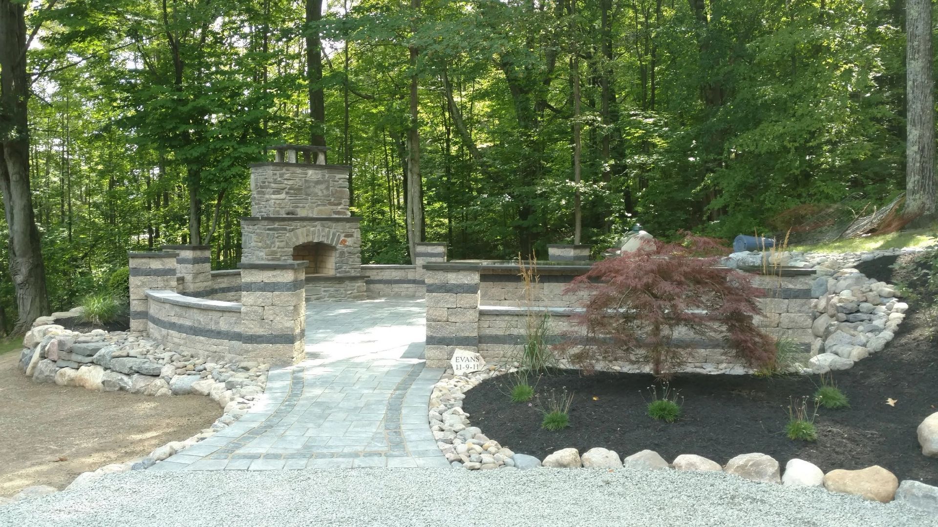 A stone walkway leading to a fireplace in the middle of a forest.