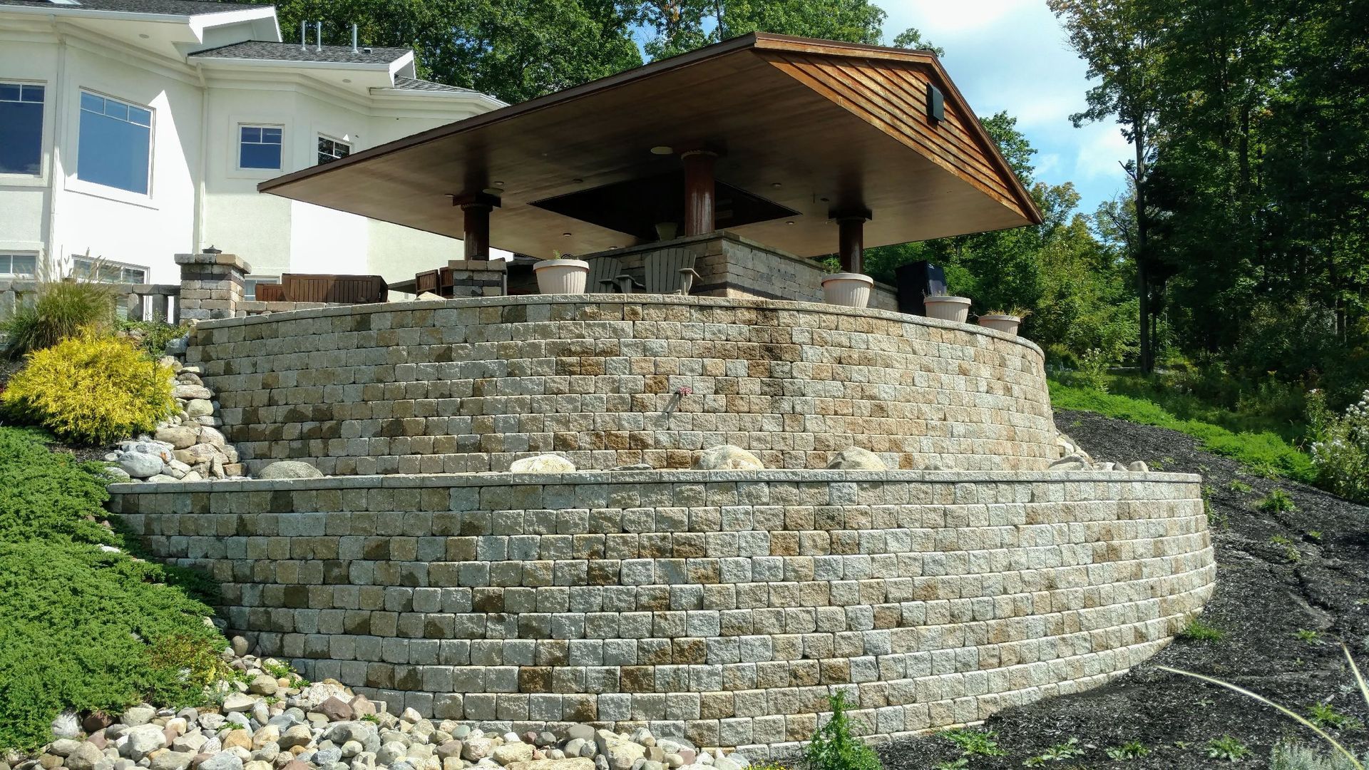 A stone wall with a gazebo on top of it in front of a house