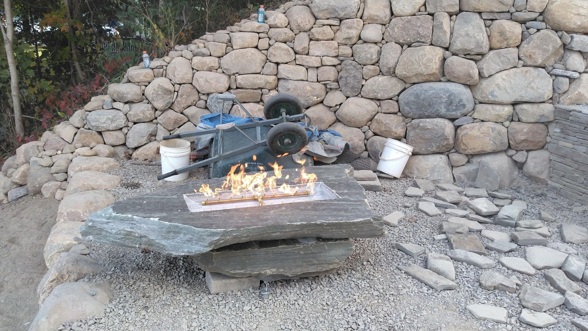 A wheelbarrow is sitting on a rock in front of a stone wall