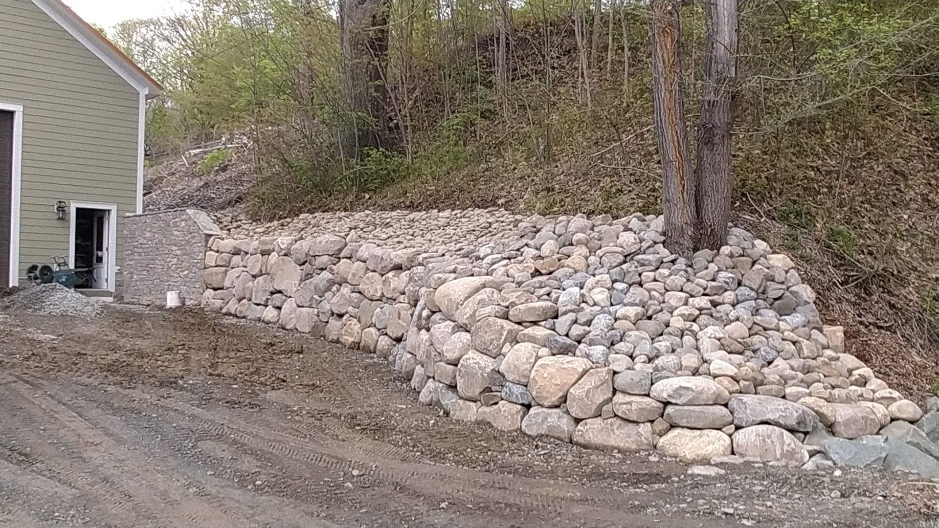 A large pile of rocks is sitting on the side of a dirt road next to a house