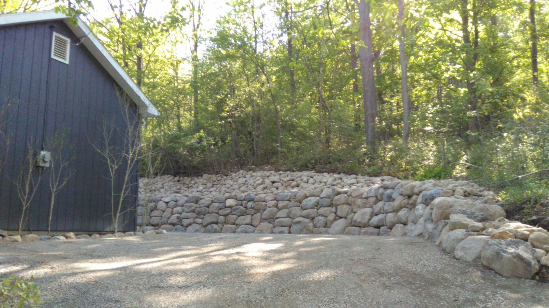 A black barn is sitting next to a stone wall in the woods