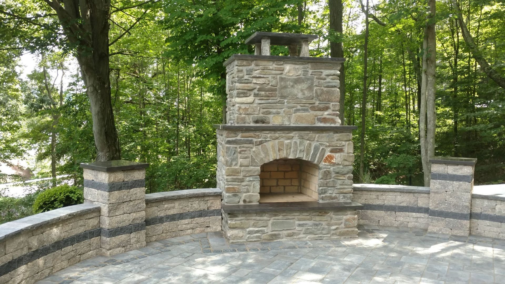 A stone fireplace is surrounded by trees on a patio