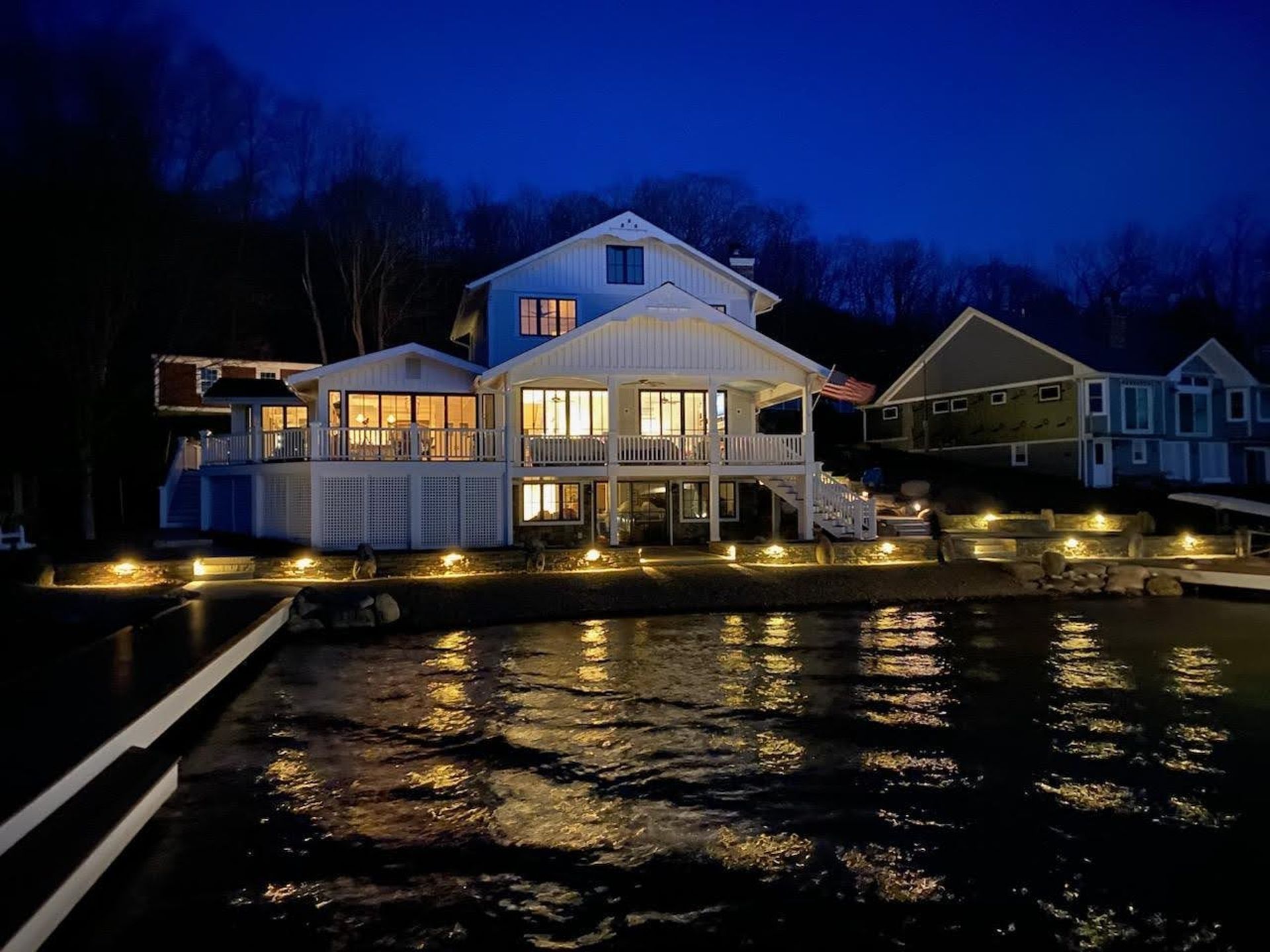 A large white house is lit up at night next to a body of water