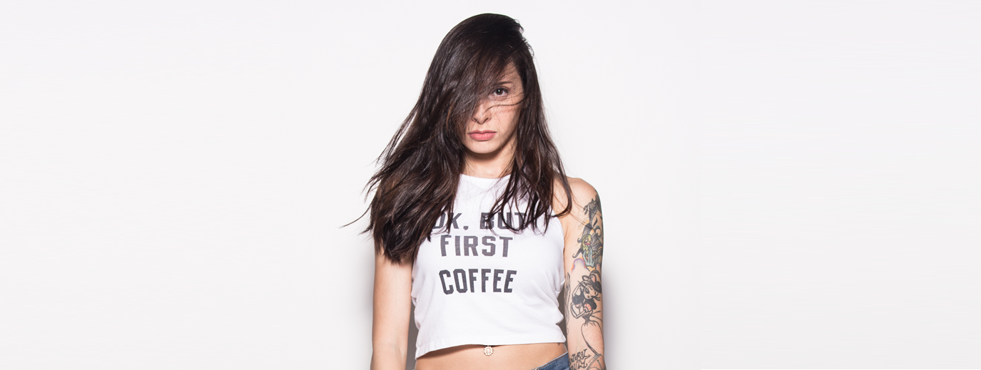 Woman with dark hair and tattoos, wearing a 