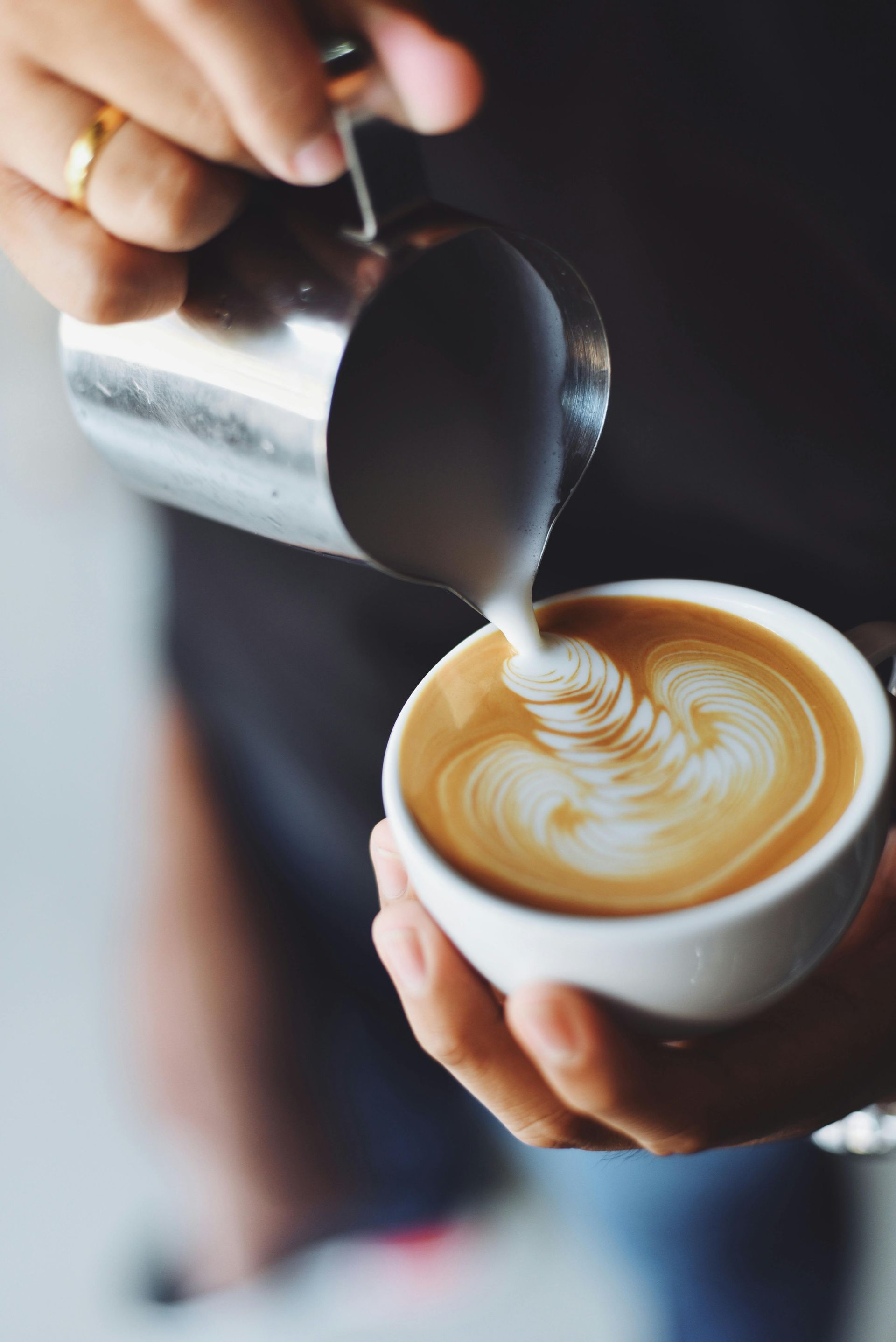 Hands pouring steamed milk into a white coffee cup, creating latte art.