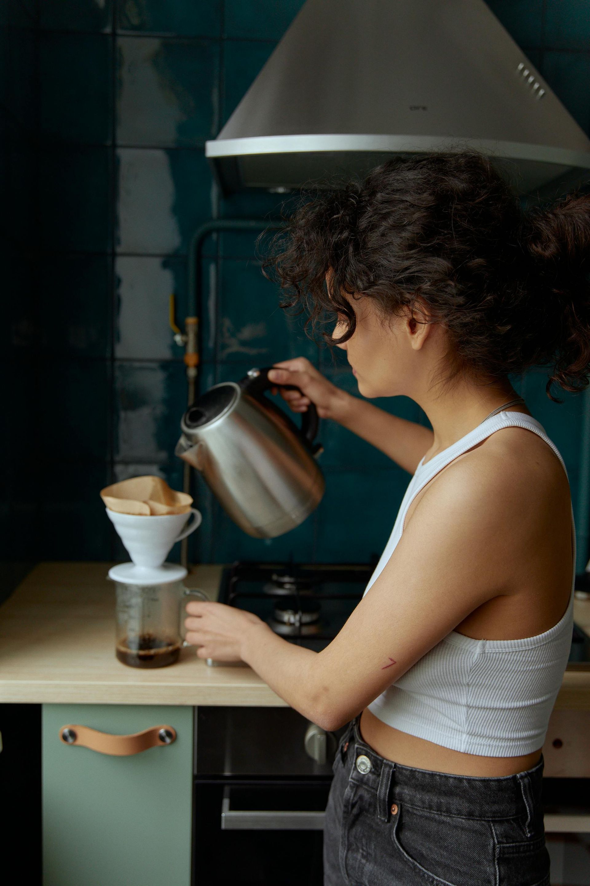 Person pouring water from a kettle into a coffee filter in a kitchen.