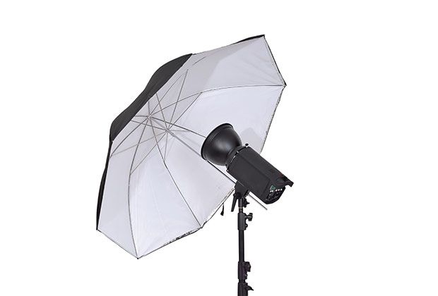 A white umbrella is sitting next to a black light on a stand.