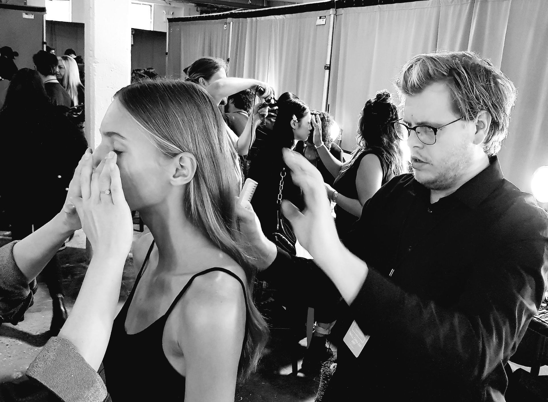 A woman is getting her makeup done by a man in a black and white photo.