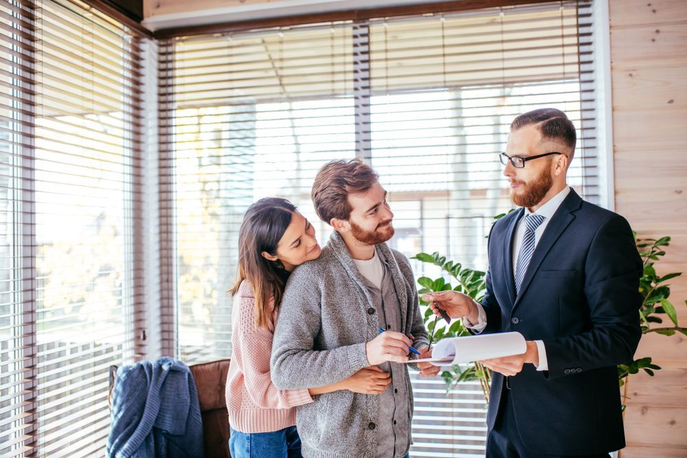 A man in a suit is talking to a couple in a living room.