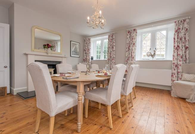 Dining room with wooden floor, table set for six, fireplace, and floral curtains.