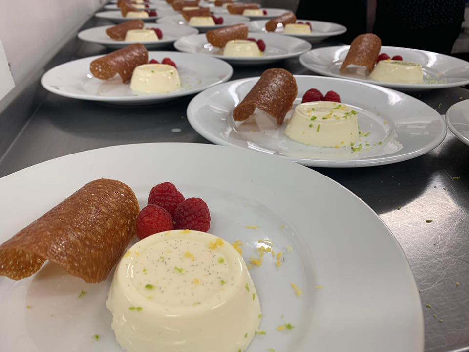 Plated desserts on a counter: panna cotta with crisp, raspberry garnish.
