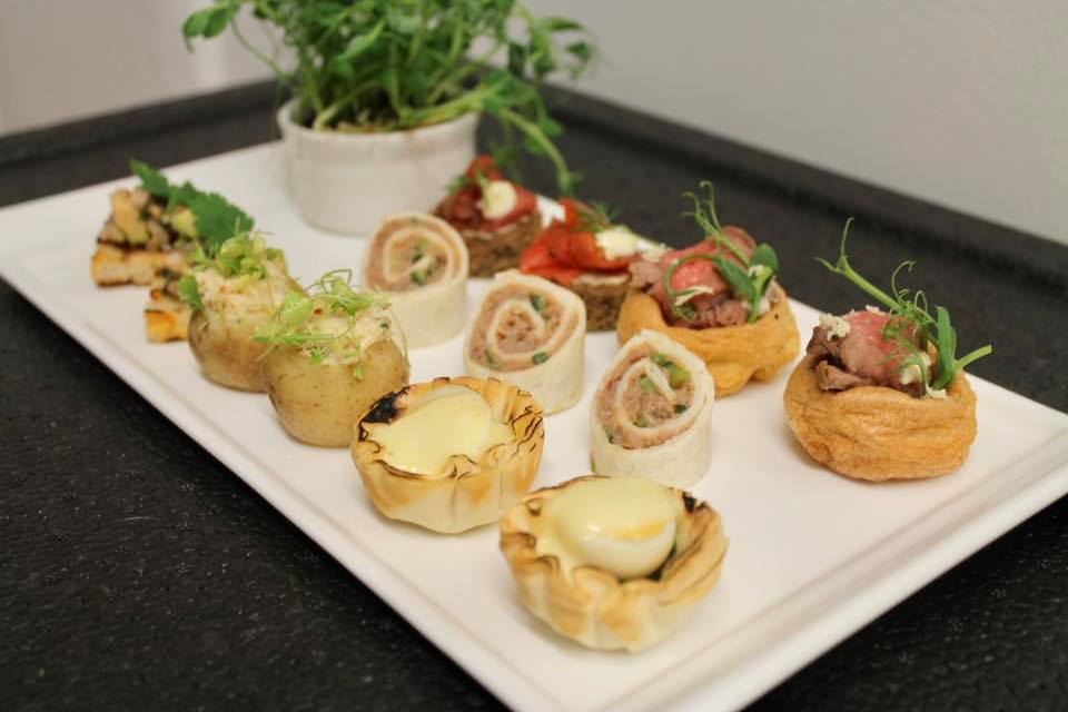 A platter of assorted appetizers, including tarts, wraps, and savory bites, garnished with greenery.