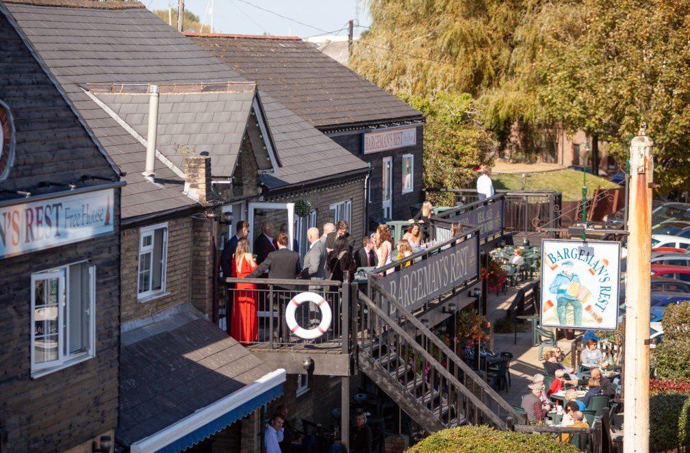 Restaurant with outdoor seating on a wooden deck; people socializing; sunny day.
