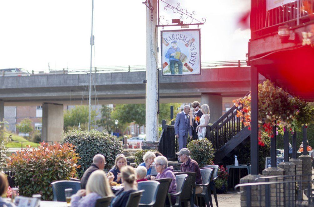 People at outdoor tables under a pub sign, with a highway overpass in the background.