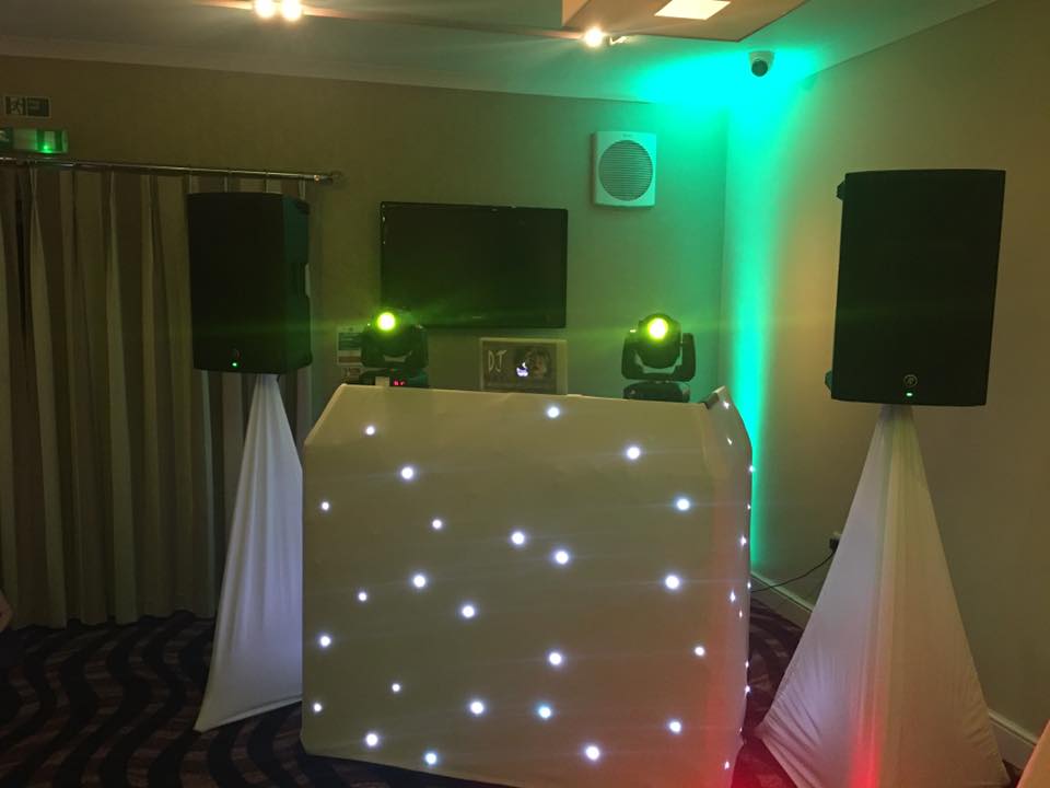 DJ setup with starry backdrop, speakers, and green stage lighting in a room.