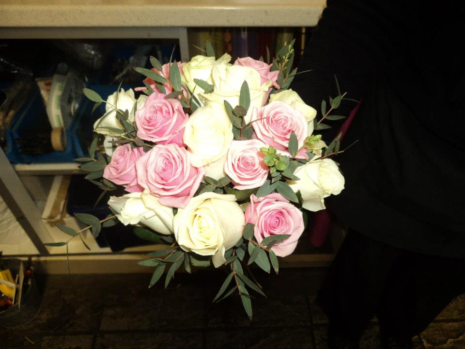 Bouquet of pink and white roses with greenery, held by a person in a dark jacket.