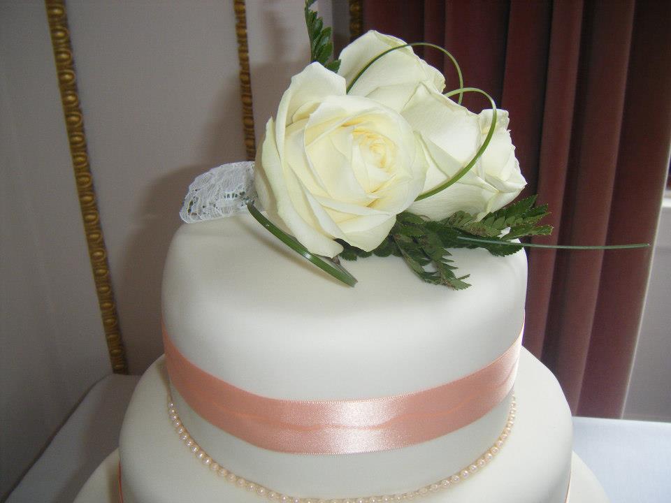 White wedding cake with peach ribbon and roses.