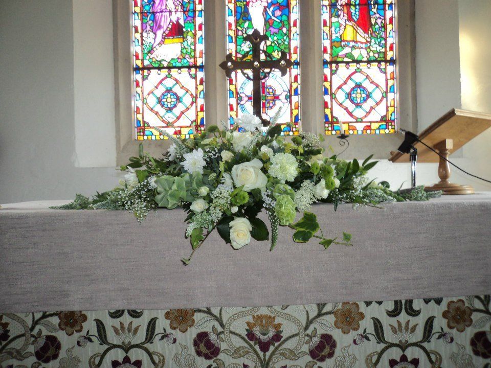Floral arrangement on altar in church, stained glass windows in background.