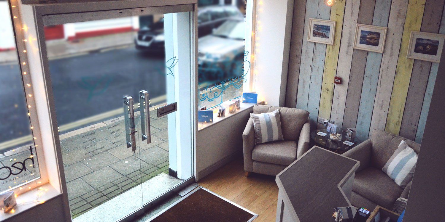 Interior shop entrance with glass door. Two armchairs and counter with striped wall decor. Street view in background.
