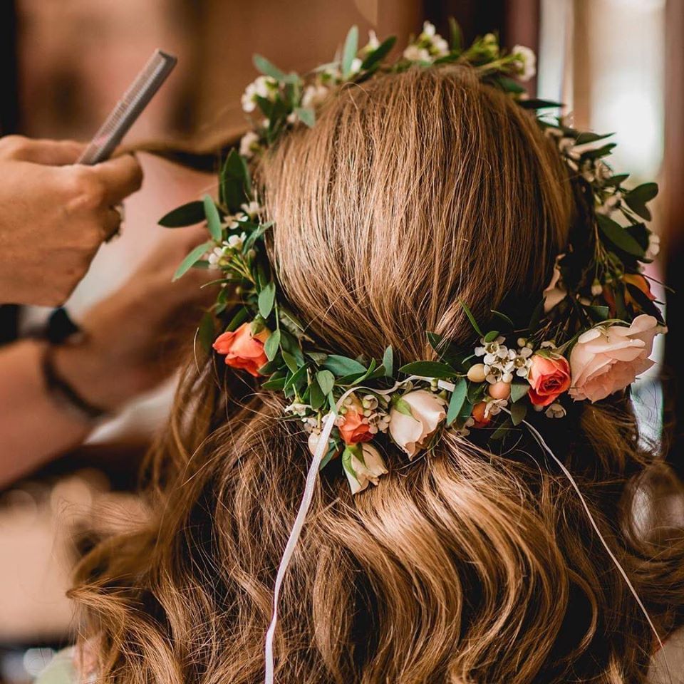 Woman's hair with floral crown; stylist works on hair with a comb.