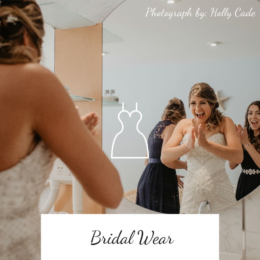 Bride in wedding dress, reflected in mirror, clapping hands with bridesmaids.