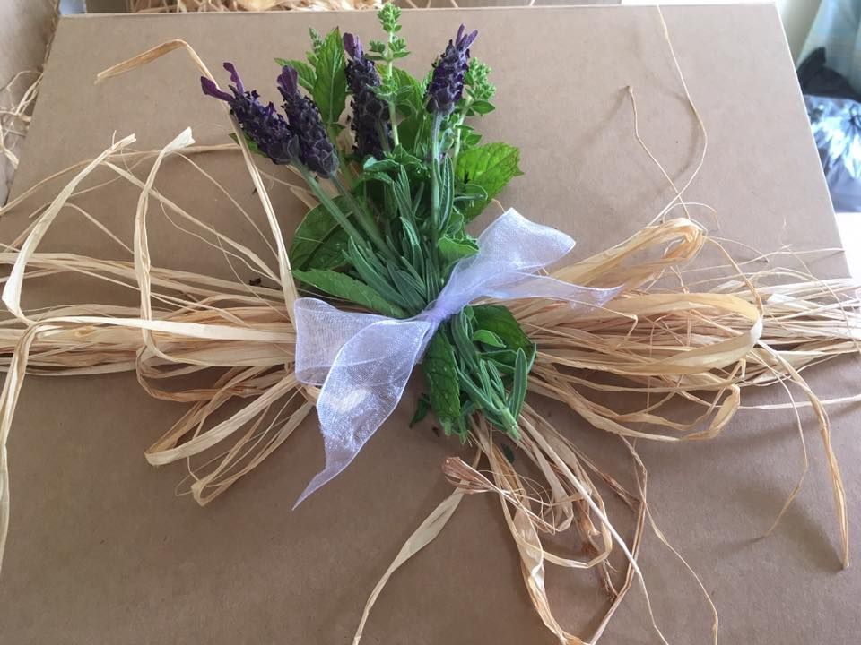 Brown package decorated with lavender, green herbs, white ribbon, and raffia.