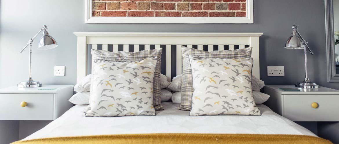 Bedroom with a white bed, gray walls, and matching nightstands with lamps. A brick wall art piece hangs above the headboard.