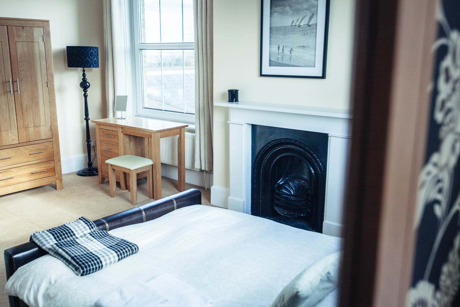 Bedroom with a bed, desk, fireplace, and wooden cabinet. Window provides natural light.