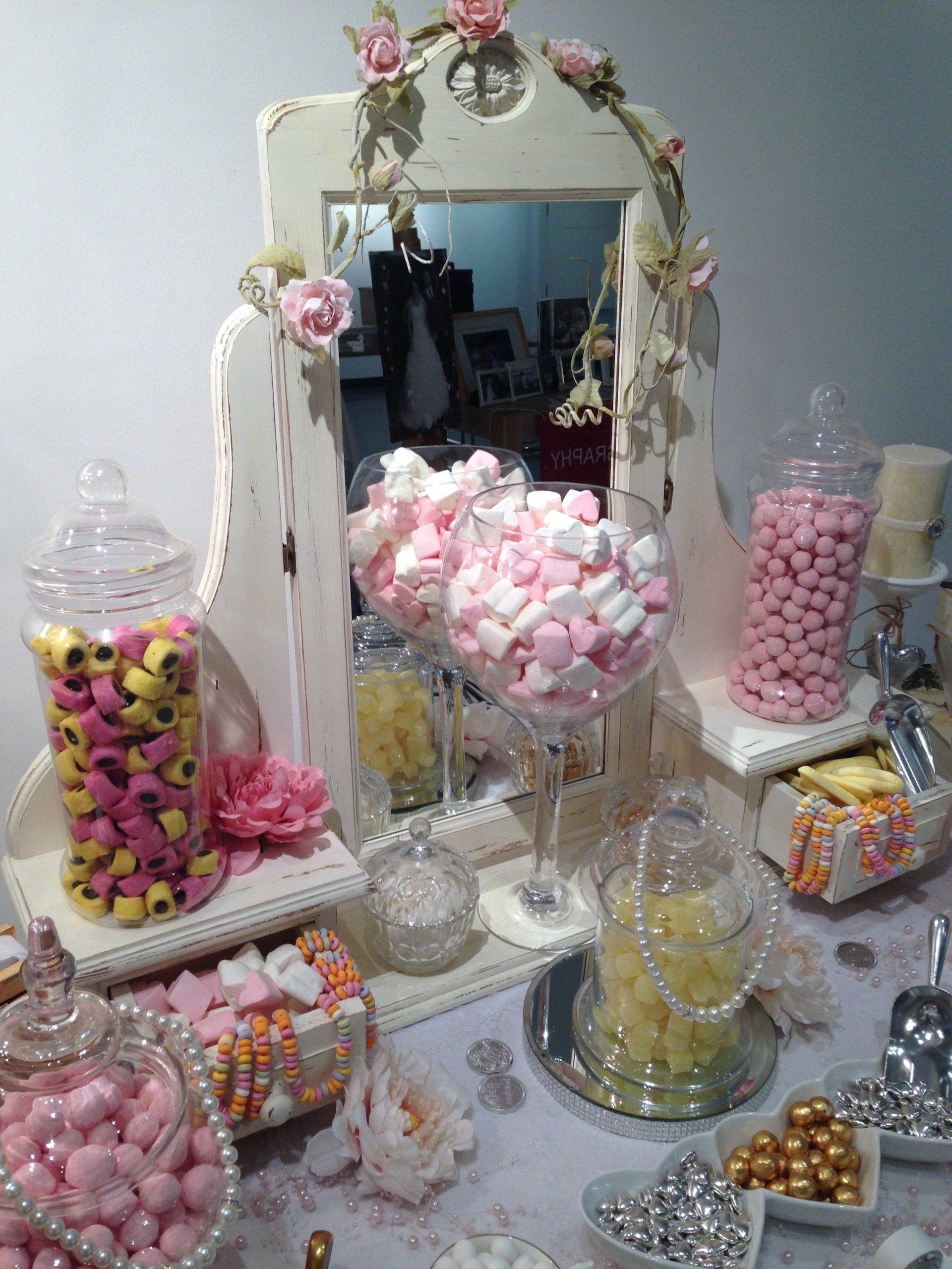 Candy buffet with jars of treats, pink and yellow sweets, and a decorative mirror.