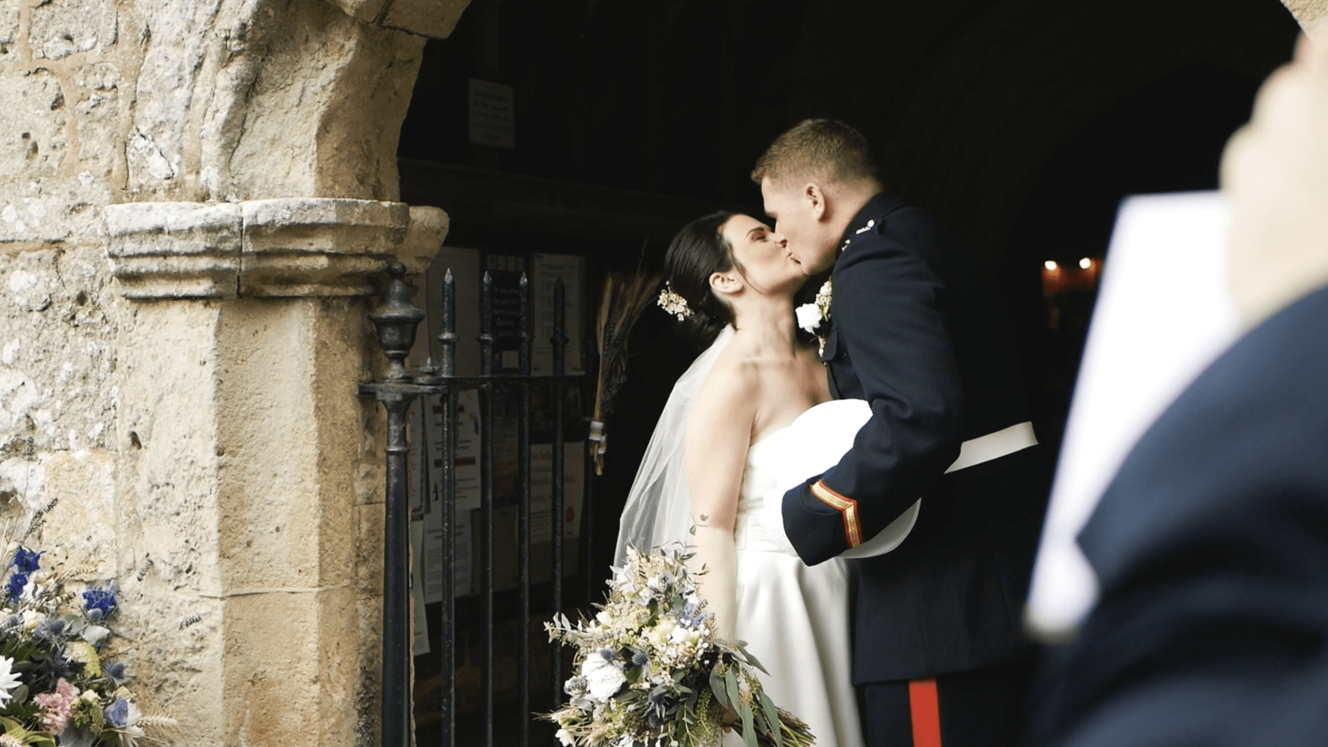 Bride and groom kiss outside a church door. The man wears a navy uniform.