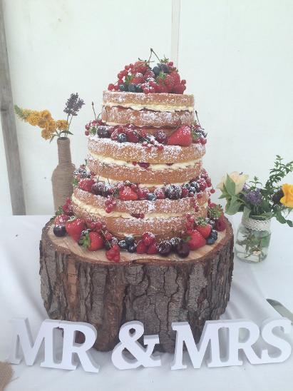 Naked cake with berries atop a wooden cake stand,