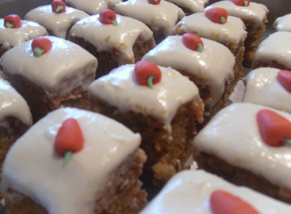 Tray of small carrot cakes with white icing and red candy carrot toppers.