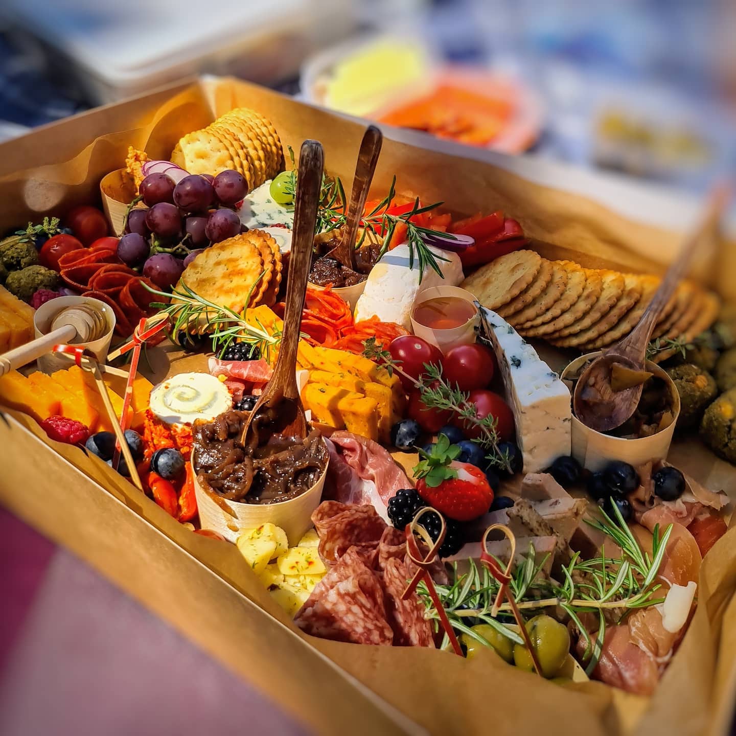 Charcuterie board with grapes, cheese, crackers, and meats, arranged in a box.