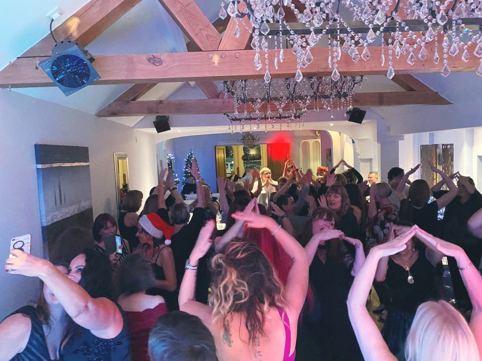 People dancing at a party under crystal chandelier. Festively lit room, arms raised in celebration.