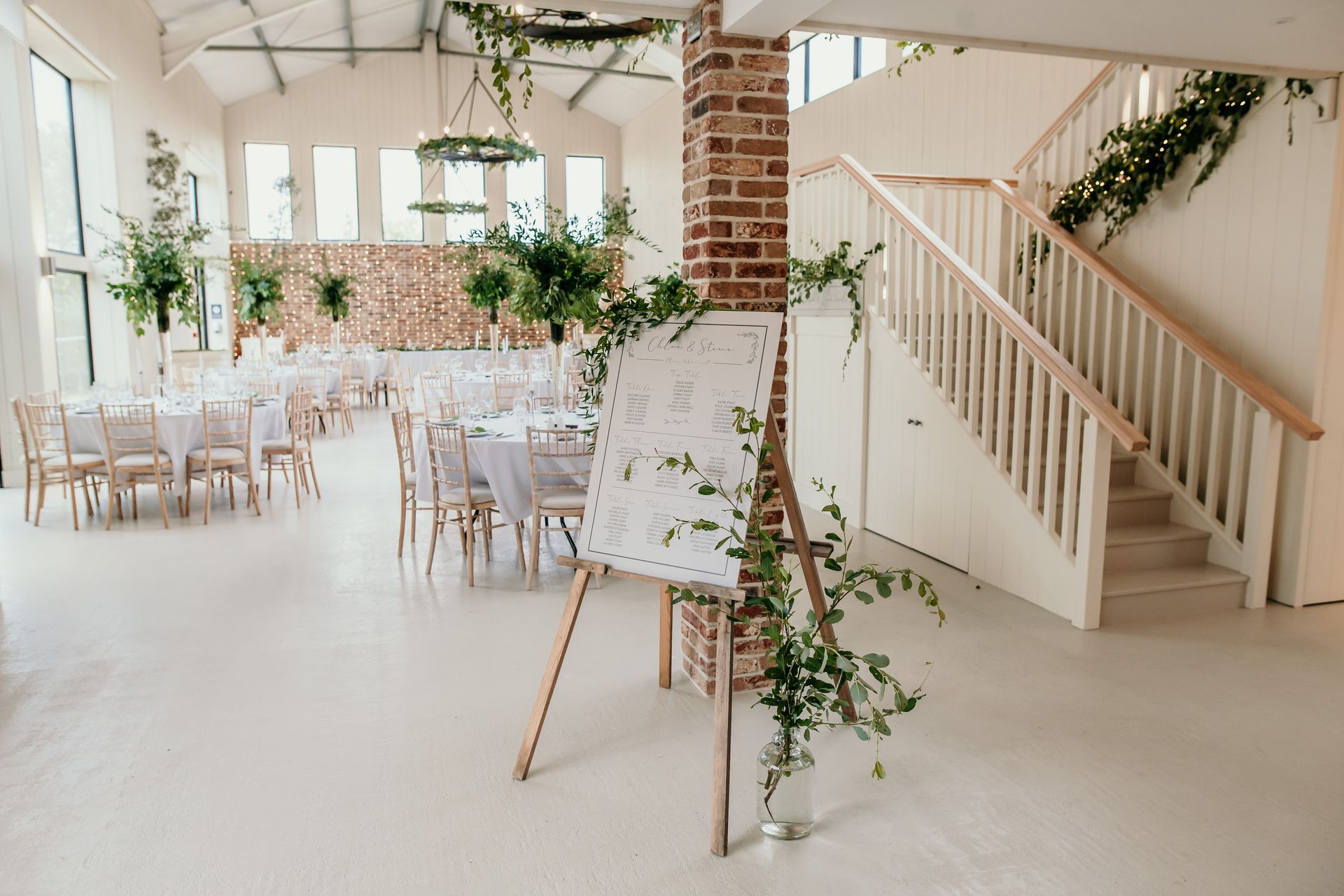 Wedding reception venue with a seating chart, greenery, and a staircase.