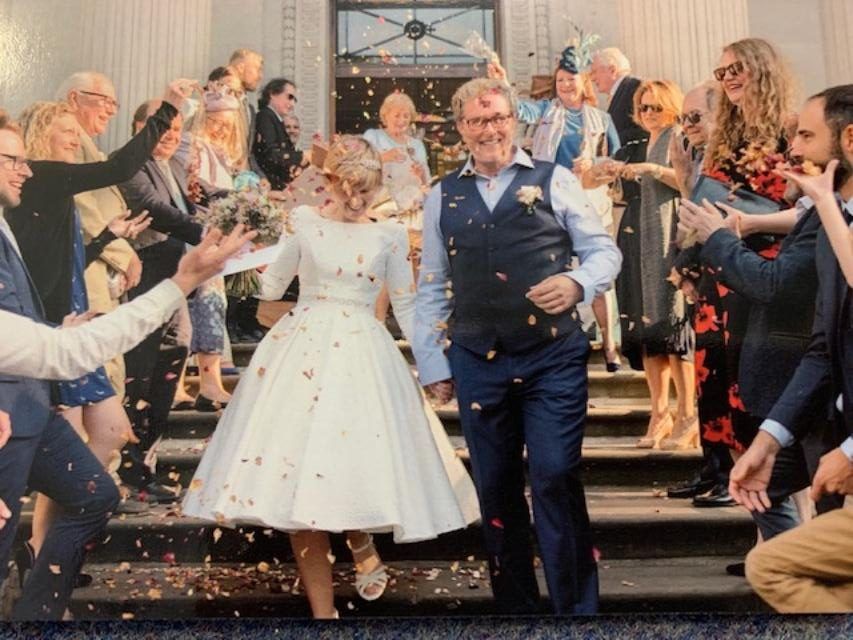 Newly married couple descends steps amid confetti, guests cheering.