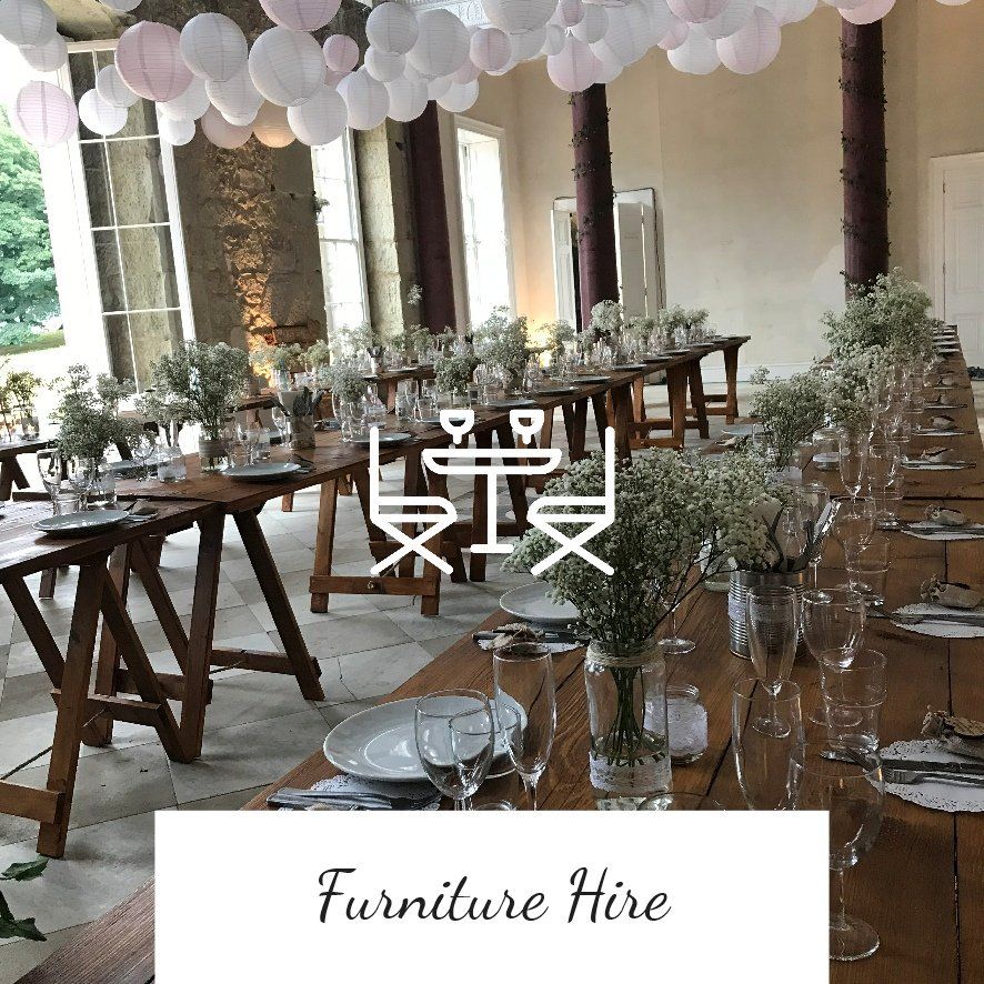 Long wooden tables set for a gathering, white floral centerpieces, paper lanterns. Furniture hire.