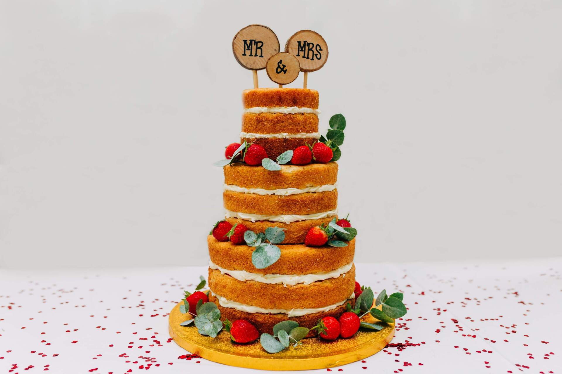 Naked wedding cake with five tiers, strawberries, greenery, and
