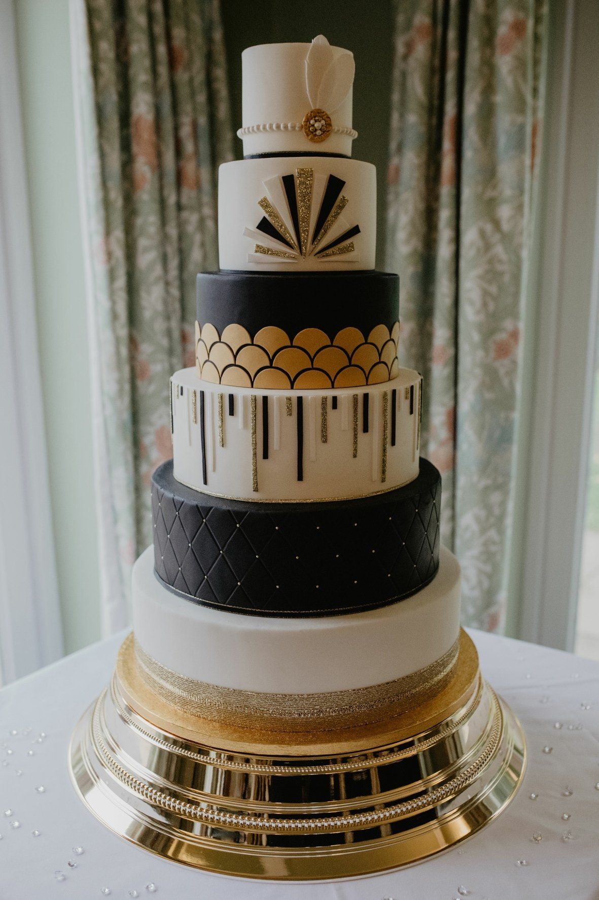 Art Deco-themed, tiered wedding cake in white, black, and gold on a gold cake stand.