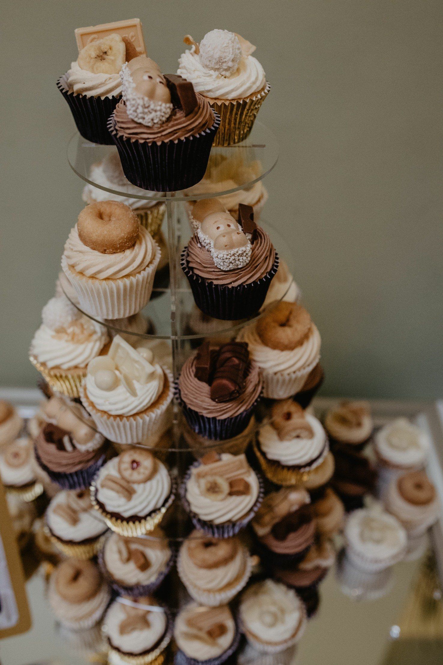 Cupcakes on a tiered stand, varying flavors and decorations, on a reflective surface.