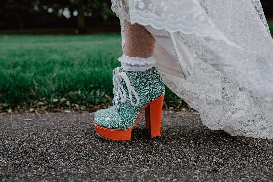 Woman's foot in green glitter boot with orange platform and heel, white lace trim, white socks.