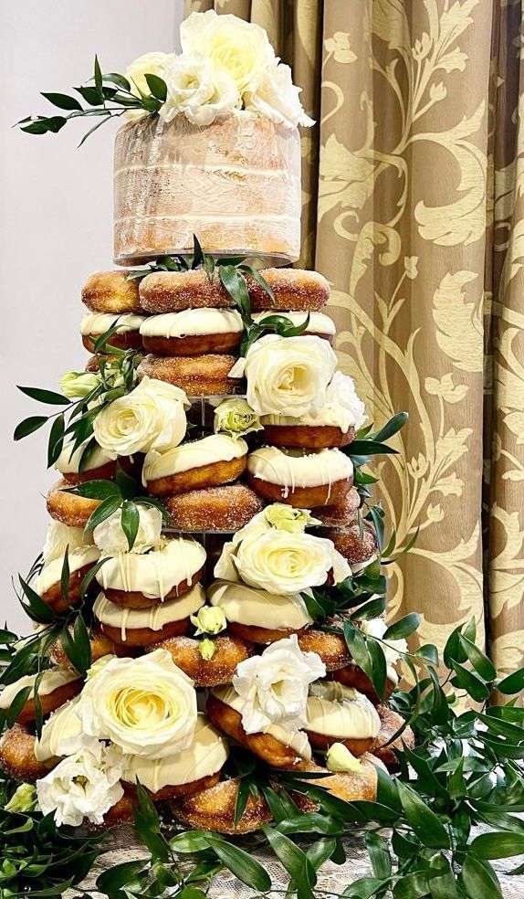 Wedding cake tower: donuts and a small cake, decorated with white flowers and greenery.